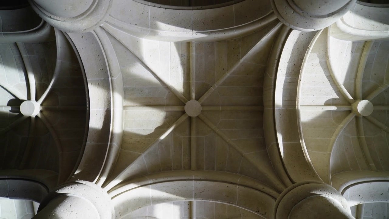 Luce solare mutevole che scivola attraverso la volta a crociera in pietra sul soffitto della cattedrale, rivelando la chiave di volta centrale.