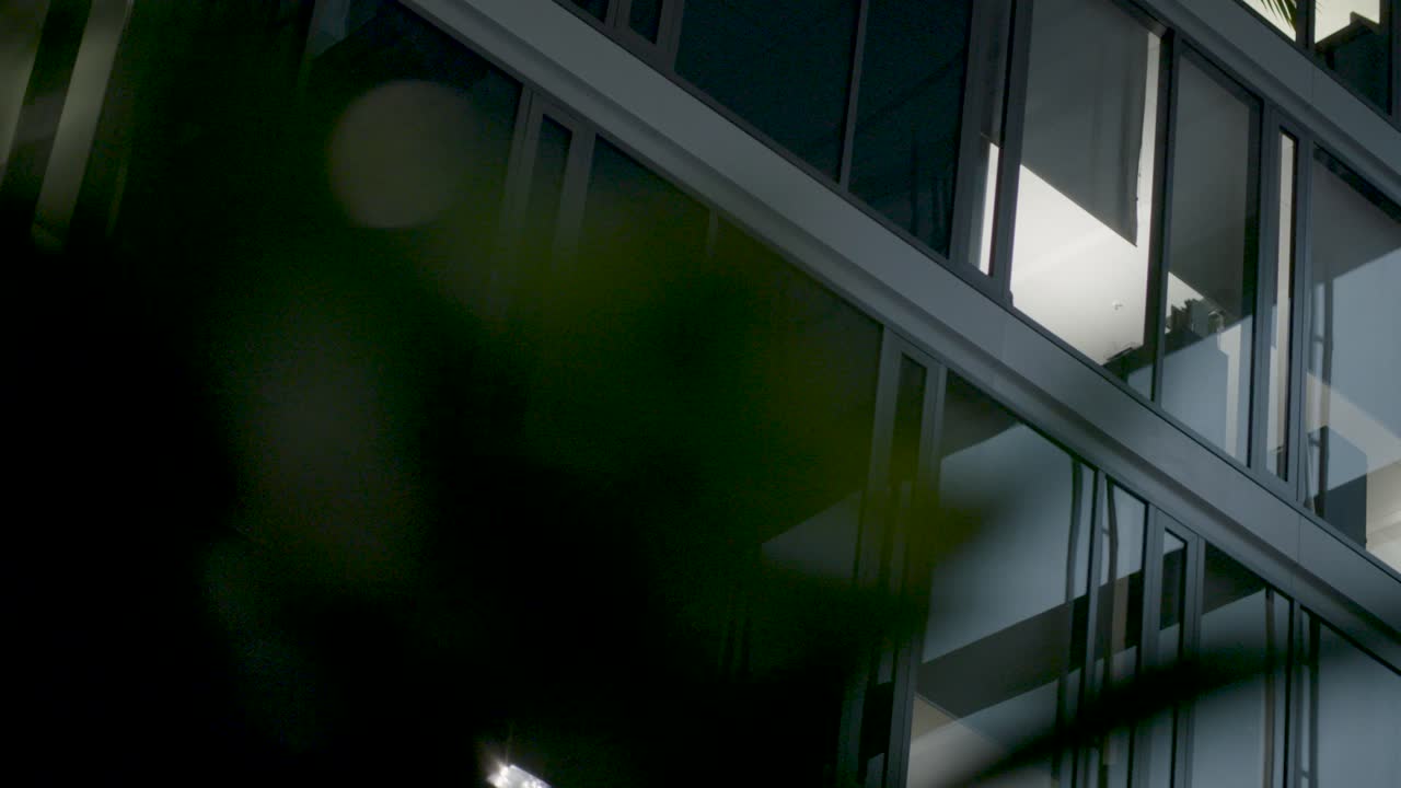 vista nocturna de la fachada iluminada de un edificio de oficinas moderno con ventanas reflectantes, toma de cámara de camiones