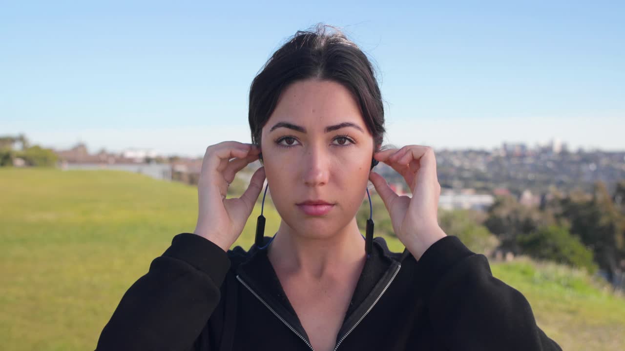 mujer euroasiática se pone los auriculares antes de salir a correr mirando a la cámara