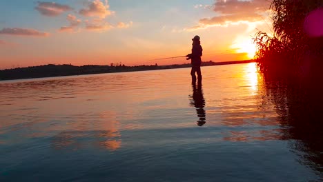 a girl fishing in a calm lake during a perfect sunset over the water