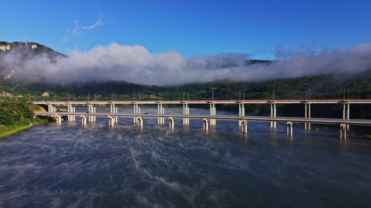 橋の下の川を霧が覆い、背景には山々が広がる。