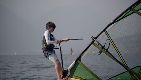 young boy raises windsurfing sail in ocean, tracking