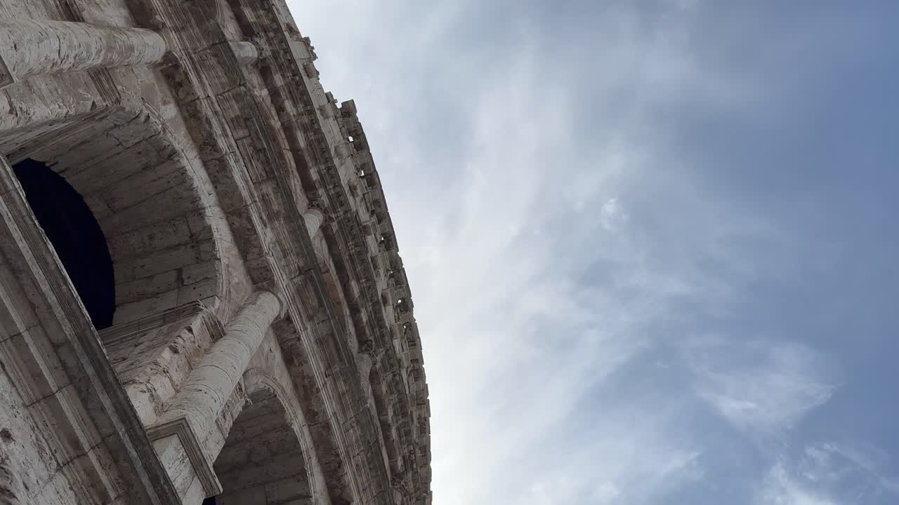 vista desde el exterior del coliseo mirando hacia arriba a un cielo azul con nubes ligeras