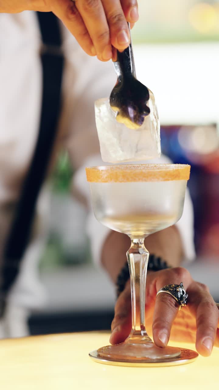 Barman che aggiunge cubetti di ghiaccio a un bicchiere da cocktail con bordo zuccherato