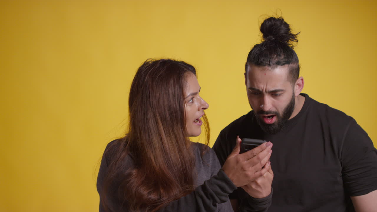 Studio Shot Of Excited Couple With Mobile Phone Celebrating Winning Money Against Yellow Background 1