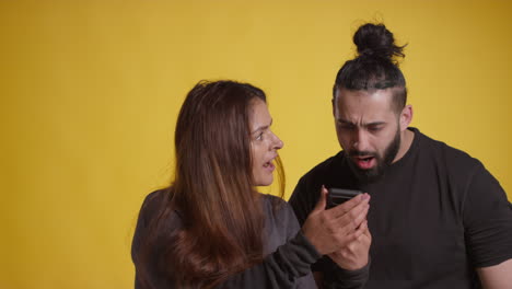 studio shot of excited couple with mobile phone celebrating winning money against yellow background 1