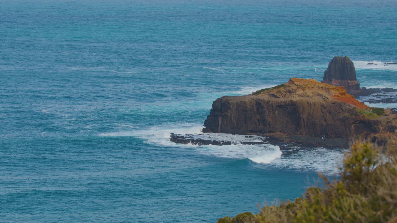 Steady wide shot of rugged cliffs, blue ocean, and gentle waves under natural daylight