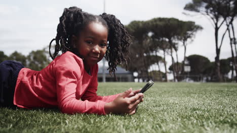 young girl enjoying outdoor time, lying on grass and using smartphone happily, copy space