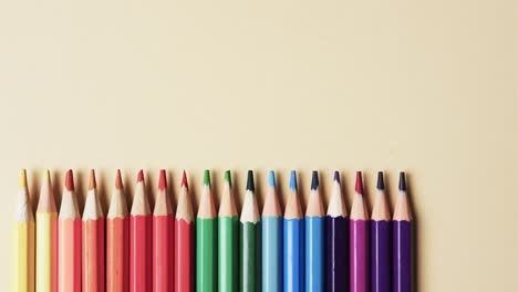 Overhead-view-of-crayons-arranged-with-copy-space-on-beige-background,-in-slow-motion