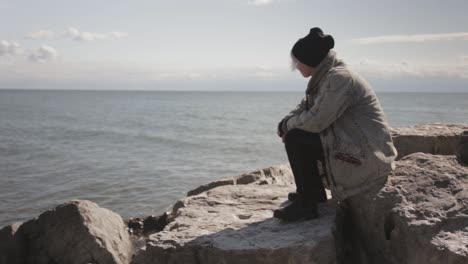 Toronto-Kanada---Eine-Frau,-Die-Allein-Auf-Dem-Großen-Felsen-Sitzt-Und-Aus-Der-Ferne-Den-Ozeanhorizont-Beobachtet---Weitwinkelaufnahme