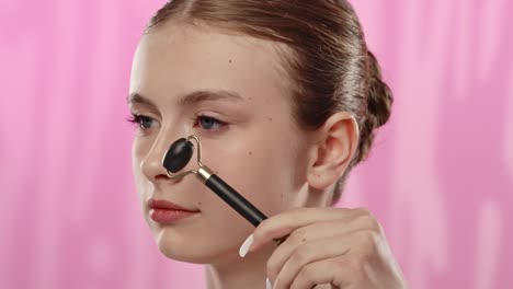young woman using facial roller on clear skin in spa environment a young woman applies a facial roller to her face in a serene spa setting with a soft pink backdrop promoting skincare routine
