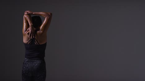 fotografía de estudio que muestra la espalda de una mujer madura con ropa de gimnasia haciendo ejercicios de estiramiento