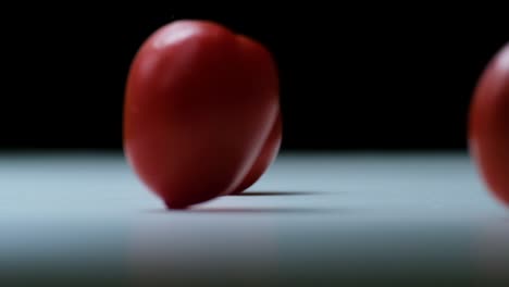 lots of different red tomatoes falling down and rolling over the white floor with black backdrop