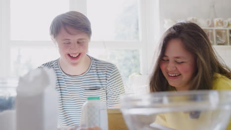 una pareja de jóvenes con síndrome de down se divierten horneando en la cocina en casa.