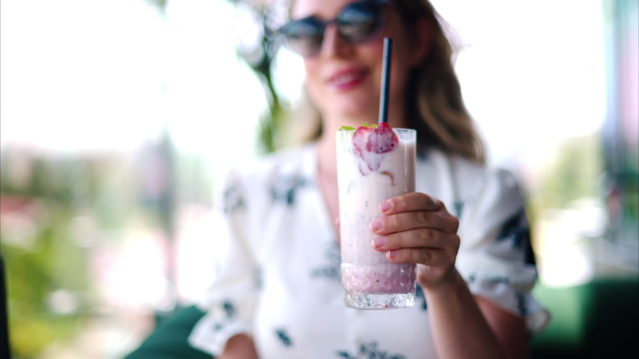 Woman presenting a strawberry drink with a black straw at a restaurant