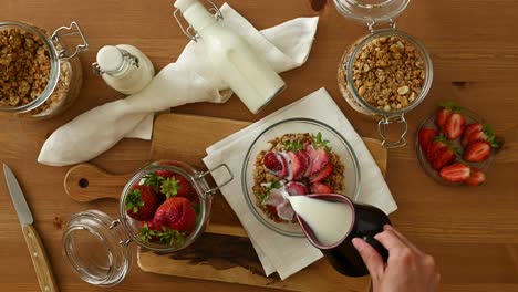 persona del cultivo añadiendo leche a un tazón de muesli con fresas