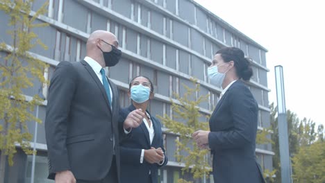 business colleagues in face masks meeting outside, greeting each other with elbows bumps and talking