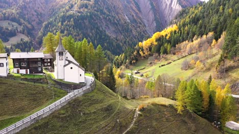 vista otoñal del bosque de alerces en suiza, con una iglesia, un pueblo y mluntais en el fondo