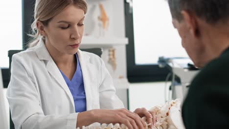 Caucasian-female-doctor-talking-with-patient-about-his-spine.