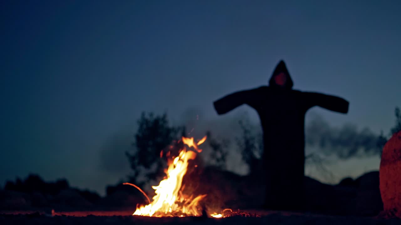 Concept of Halloween and witchcraft. Black witch in a mantle stays in front of fire
