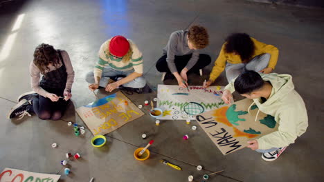 top view of young environmental activists painting placards sitting on the floor