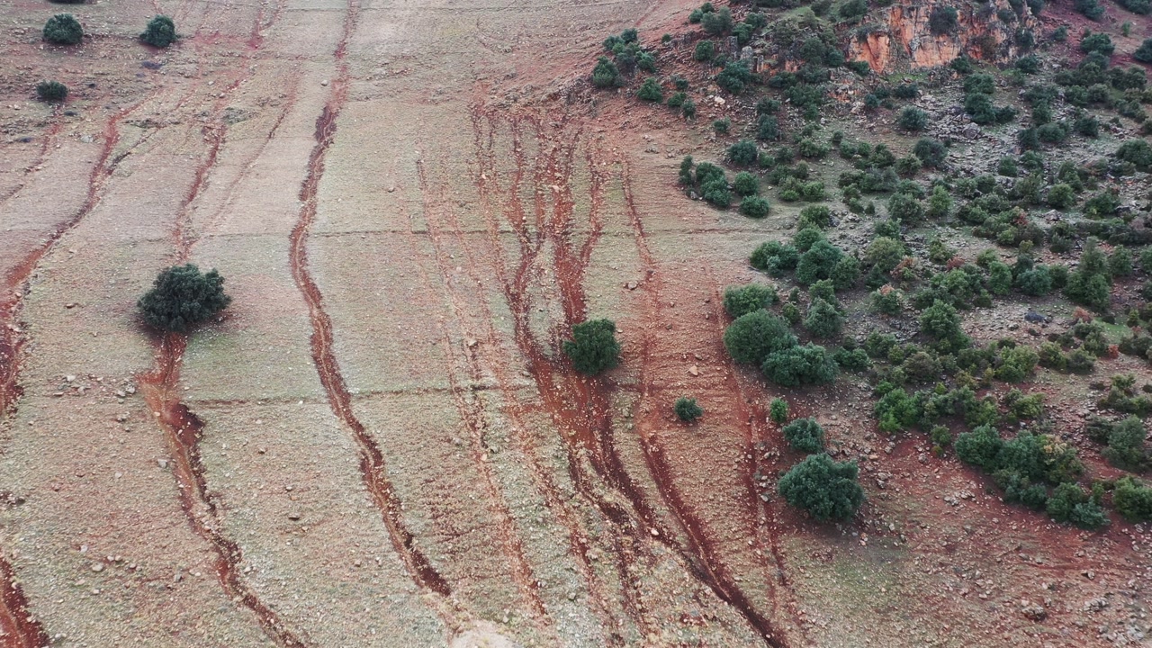 Cinematic 4K drone shot showing severe soil erosion patterns and reddish earth on a mountain slope in the Middle Atlas, Morocco. Ideal for environmental and geography projects.