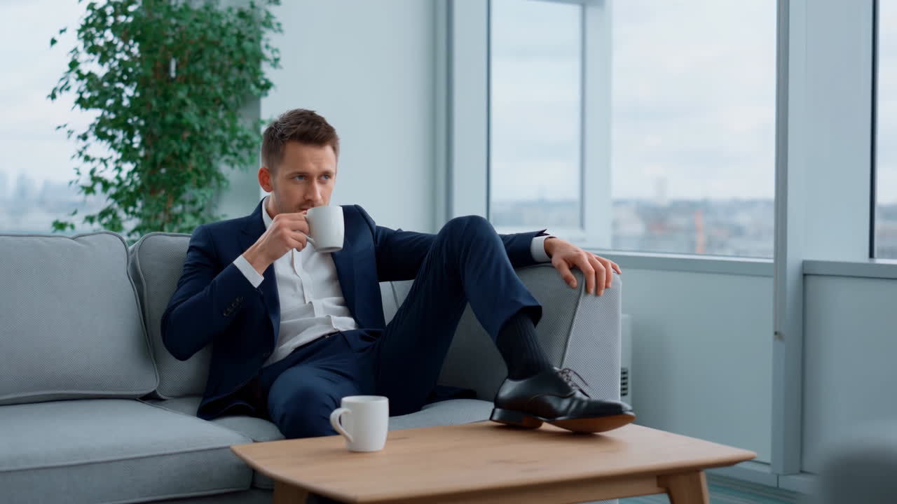 Forretningsmand slapper af på sofaen og drikker kaffe på moderne kontor
