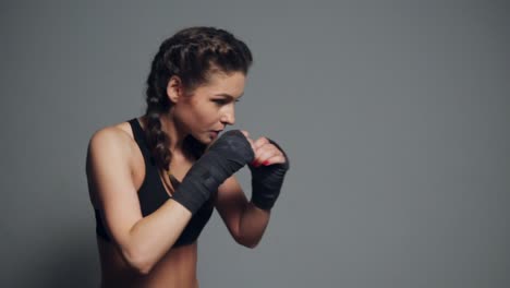 Mujer-Joven-Entrenando-Con-Las-Manos-Envueltas-En-Cintas-De-Boxeo-Aisladas-Sobre-Fondo-Gris.-Tiro-En-Cámara-Lenta