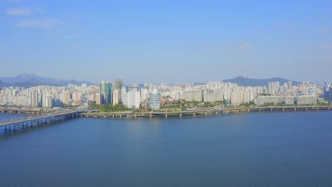 drone shot traveling forward above the han river toward a residential district in seoul city during the day