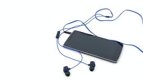 slow panning movement over black smartphone with connected sports earphones on white background