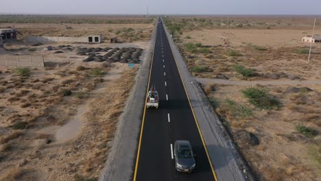 aerial over along road through desert plains in balochistan with truck parked up and cars going past