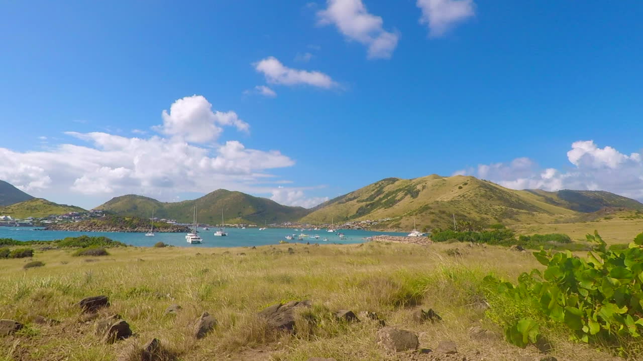 Pinel Island, Saint Martin showing vibrant grass, bay with anchored sailboats, and mountains in the background. Perfect of travel, relaxation, and nature projects