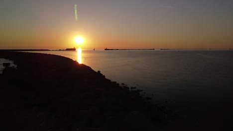 Beautiful-aerial-vibrant-high-contrast-sunset-over-calm-Baltic-sea,-rock-pier-at-Port-of-Liepaja-,-wide-angle-drone-shot-moving-backwards