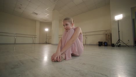 a group of young ballet students in black dancewear practicing positions in a spacious ballet studio with wooden flooring and wall-mounted barres. focused expressions and synchronized movements.