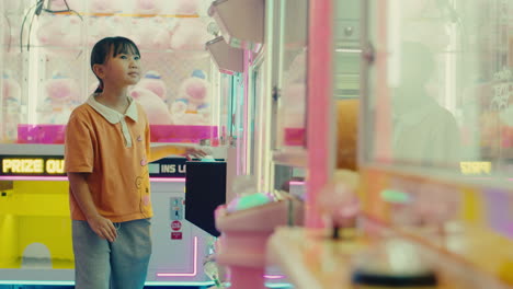 joven niña asiática linda caminando en la sala de juegos admirando la máquina de juegos de arcade en el parque de atracciones