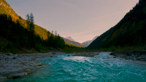 Mountain-river-evening,-clear-blue-water-rushing-by-vibrant-colorful-autumn-trees-in-the-sun