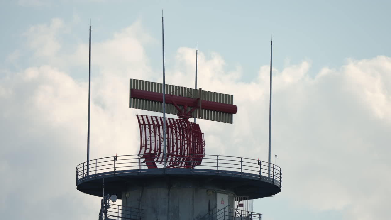 Communication tower features radar equipment and antennas, rising against a backdrop of fluffy clouds, showcasing modern technology and engineering