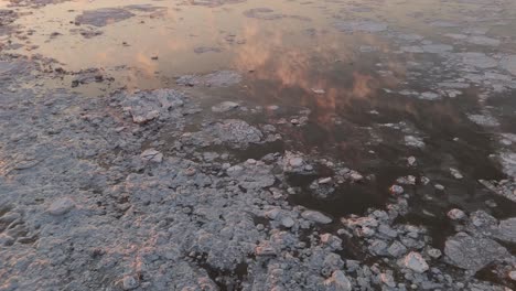 Slow-Aerial-Tracking-Shot-of-Golden-Clouds-Floating-over-Ice-Formations-on-Frozen-Lake