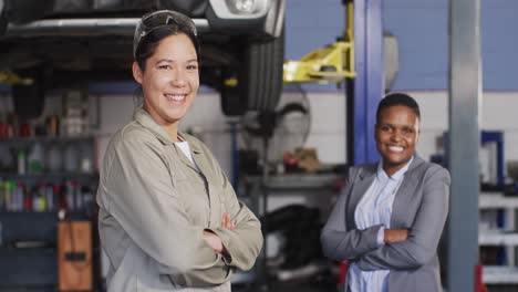 Video-of-two-diverse-happy-female-car-mechanic-and-business-owner-looking-at-camera