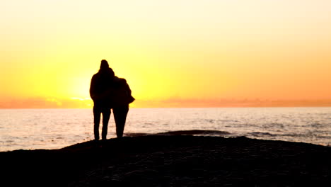 silhouette of young couple in love against golden sunset sky over ocean