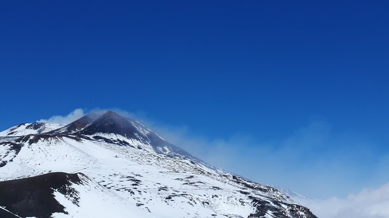 smoke comes from the  snow-capped summit of the volcano Etna on the island of sicily in Italy, nice and sunny weather, blue sky (timelapse)