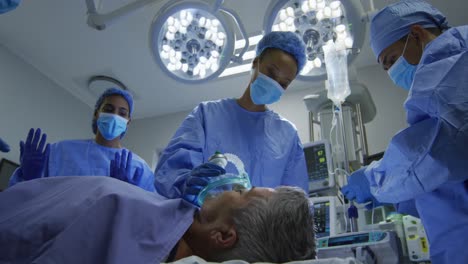 Mixed-race-surgeons-wearing-protective-clothing-putting-patient-to-sleep-in-operating-theatre