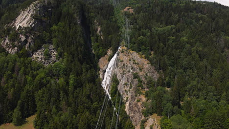 cables eléctricos sobre la montaña alpina con bosque verde y cascada en el fondo en italia