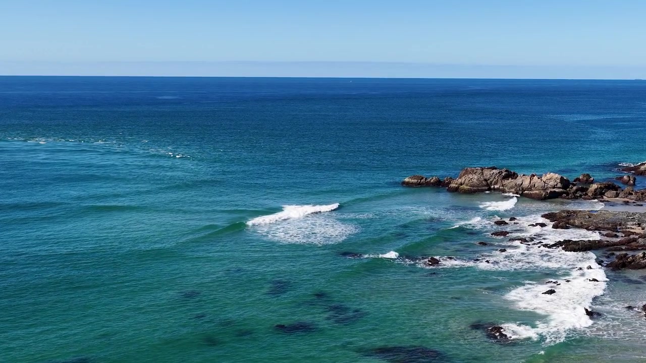 Ampia inquadratura di onde oceaniche turchesi che si infrangono su rocce scure a South West Rocks, Australia