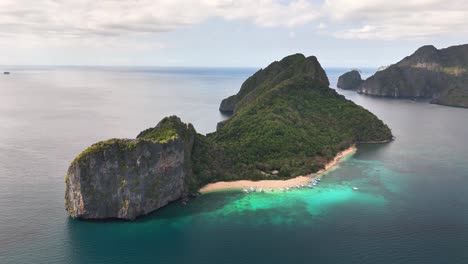 tropical duiklocatie helicopter island in the philippines features crystal-clear waters, white sand beach, dense green cliffs, and anchored boats along a serene and scenic coastal area
