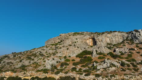 drone flying backwards away from a mountain with a cave, sunrise in greece