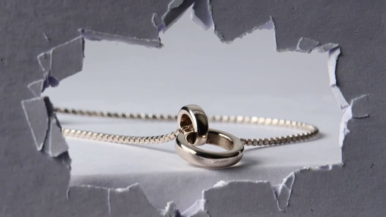 Sliding chain slider nudging two silver rings across white tabletop to reveal metal highlights
