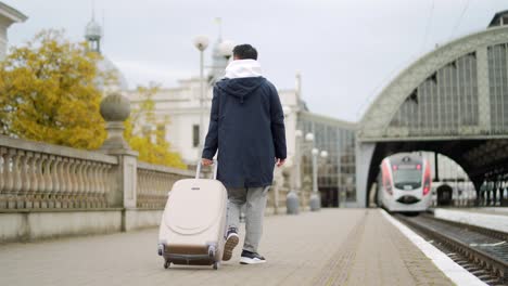 man asian passenger arrives or departure by train home, with suitcase, tourist at the railway train station male voyageur goes on the platform.