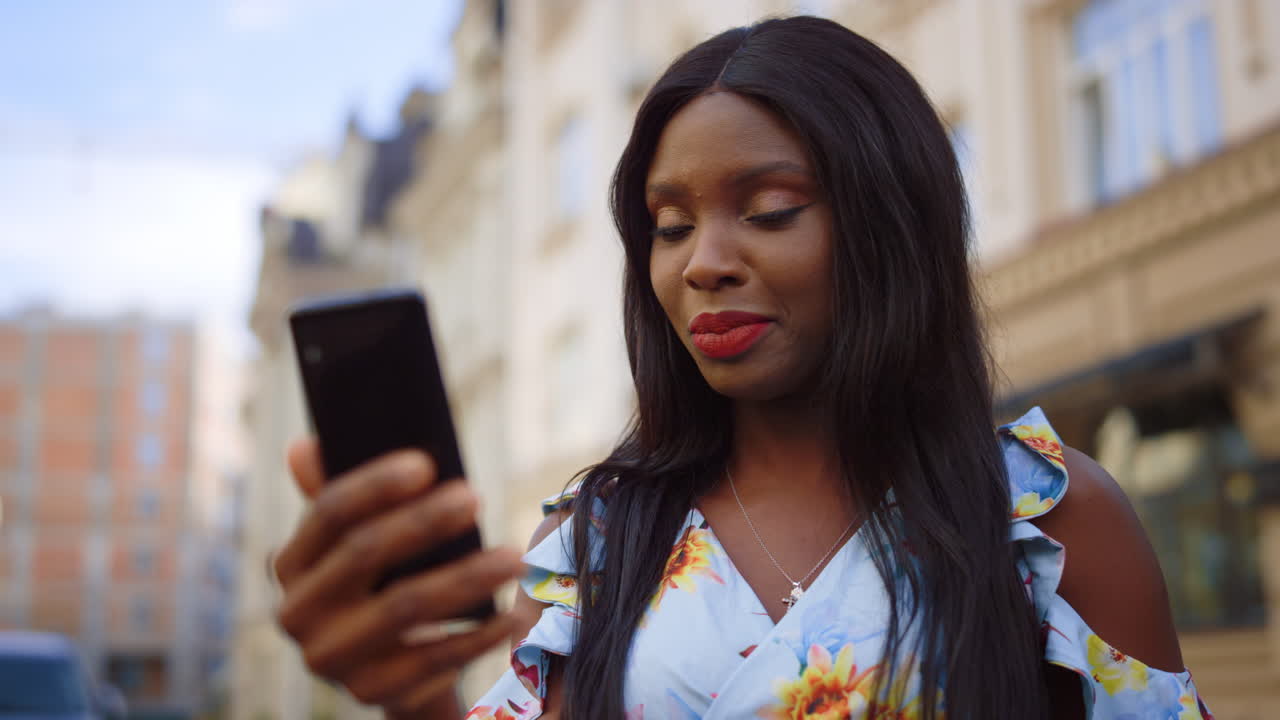 Smiling afro girl speaking on street. African woman having video call outdoors