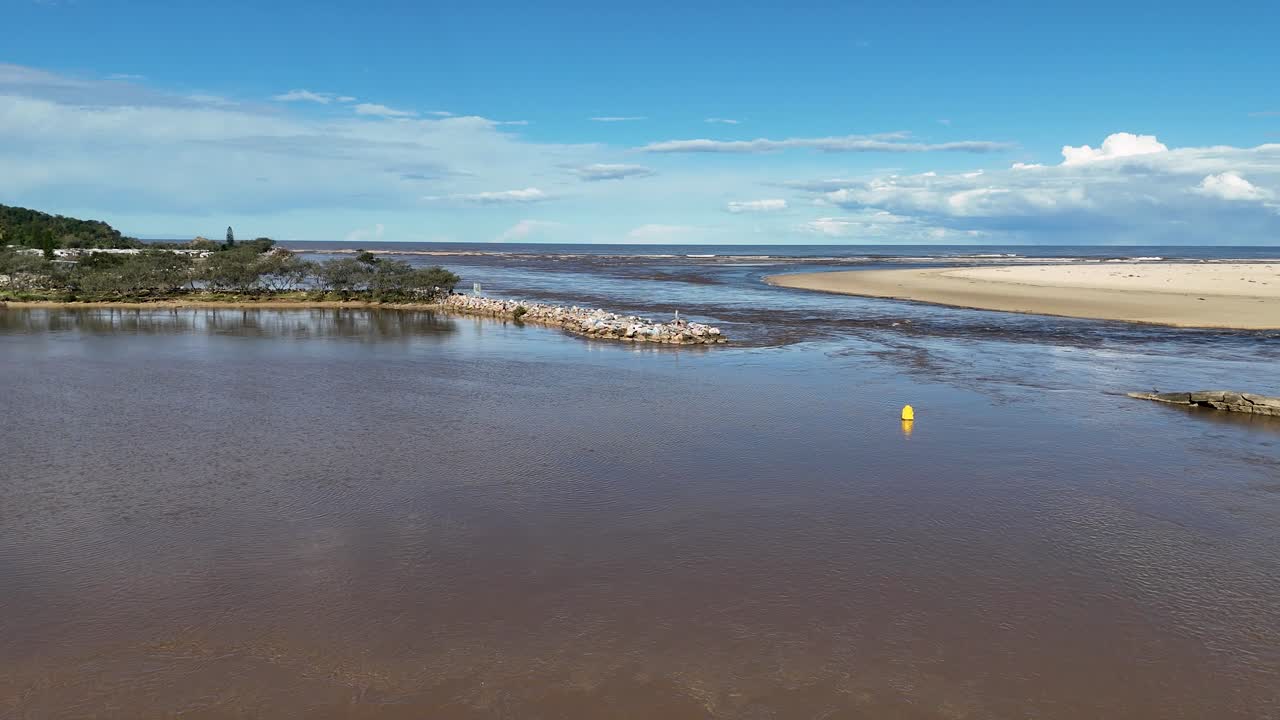 Yellow buoy drifts downstream in wide estuary under clear blue sky and bright daylight